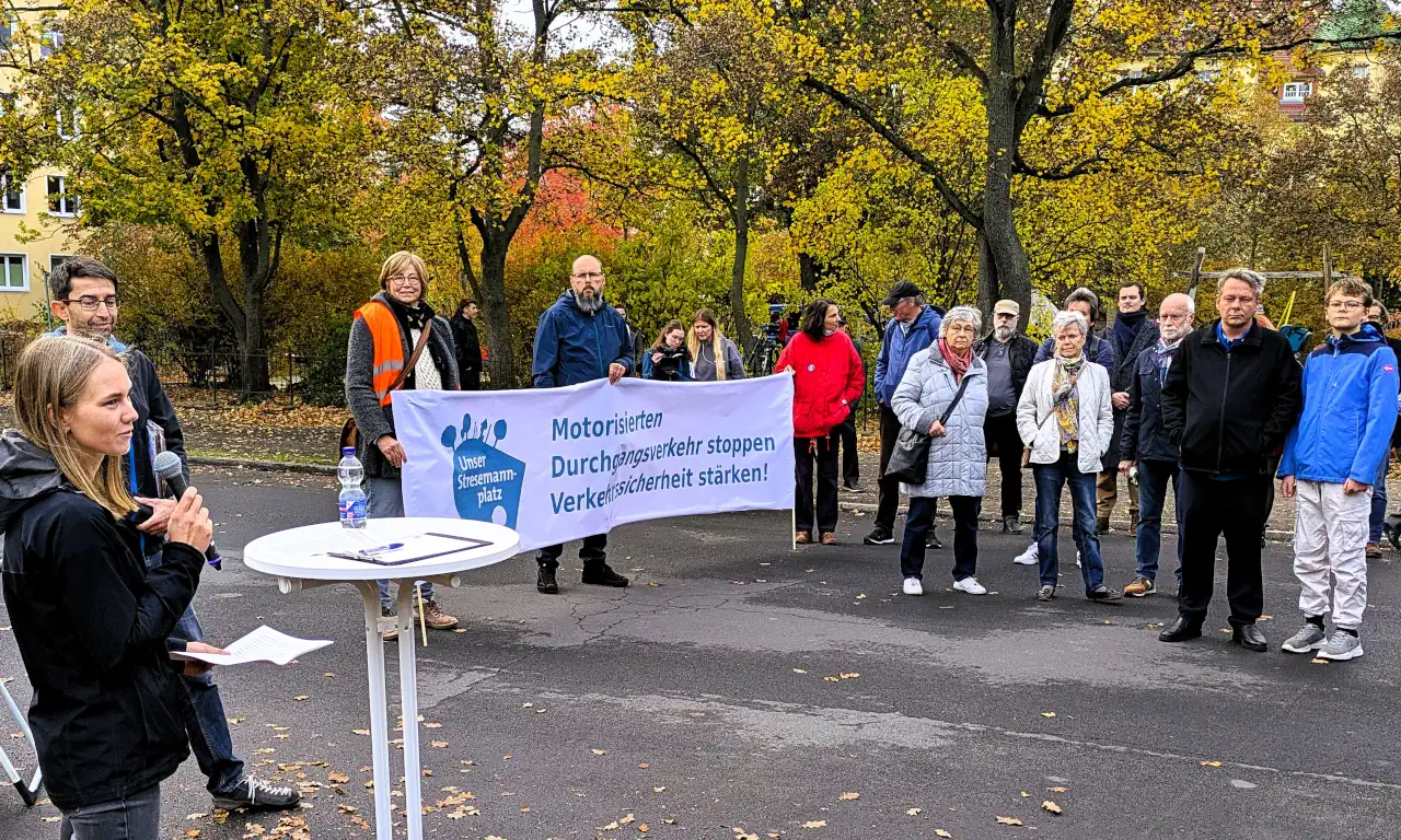 Herbstliche Kundgebung am Stresemannplatz: Bürger stehen auf der gesperrten Straße und hören Rednern zu, um sich für Bürgerbeteiligung, Verkehrswende und die Neugestaltung des öffentlichen Raums einzusetzen. Im Hintergrund sind Bäume mit gelbem Herbstlaub und historische Gebäude sichtbar.